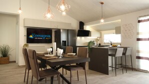 Une cuisine moderne dotée d’un îlot central, d’un coin repas avec une table et des chaises en bois foncé, et d’un téléviseur fixé au mur.