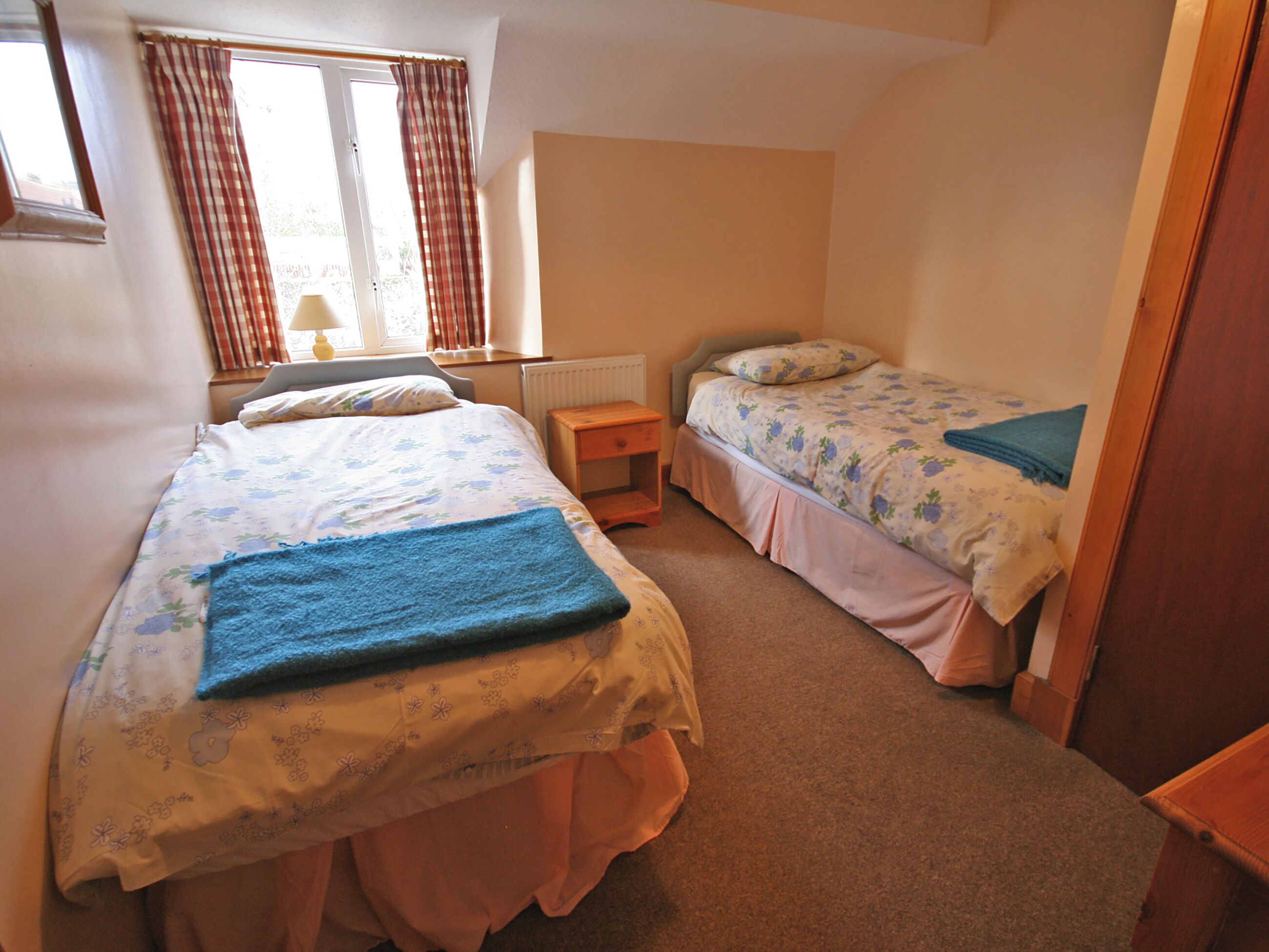 A bedroom with two single beds, a nightstand, a window with curtains, and a radiator.