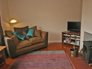 Een gezellige woonkamer met een bruine bank, teal kussens, een flatscreen televisie, een boekenkast en een houtkachel.