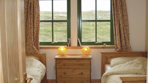 A room with two beds, a wooden dresser, and two windows with curtains.