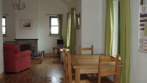 A living room with a fireplace, a dining table with chairs, a red sofa, and a television on a stand.