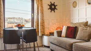 A living room with a sofa, a dining table with chairs, a ship's wheel decoration, and a view of buildings through a window. - Situated in Whitby’s old town. (Whitby)