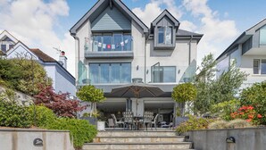 A two-story house with a balcony, outdoor seating area, and steps leading to the entrance. - 1 bedroom accommodation in 3 Coombe Close (3 Coombe Close)