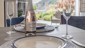 A table set for dining with a bottle of sparkling rose wine, two glasses, and a view of the outdoors. - 1 bedroom accommodation in 3 Coombe Close (3 Coombe Close)