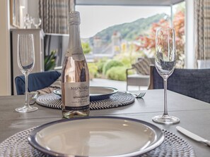 Mesa lista para cenar con una botella de vino rosado espumoso, dos copas y vistas al exterior.