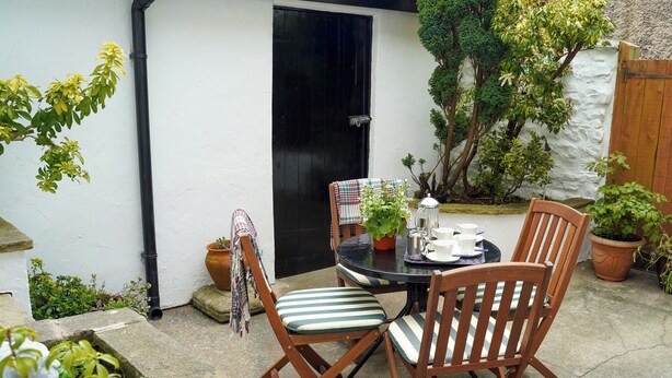 Une terrasse avec une table ronde, quatre chaises en bois et une plante en pot.
