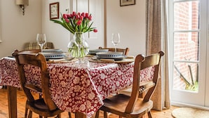 Ett matbord med ett blommigt bordsduk, omgivet av trästolar, dukat med tallrikar, skålar och glas.