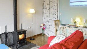 Un salon chaleureux avec un poêle à bois, un canapé rouge, une table avec une lampe et une fenêtre donnant sur un beau paysage.