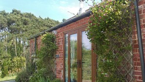 Un bâtiment en briques doté d’une porte et de fenêtres en verre, entouré de verdure et bordé d’un chemin pavé.