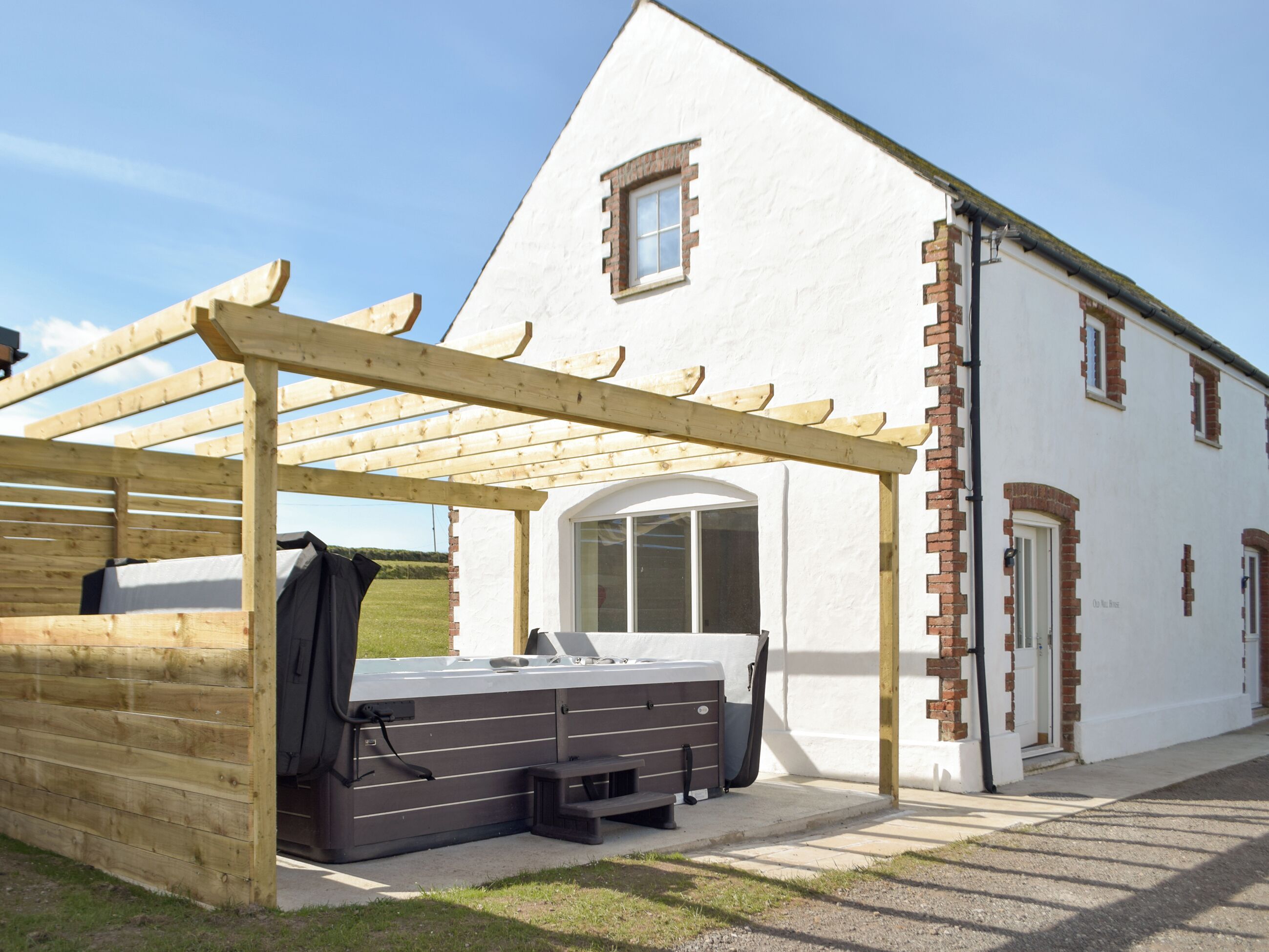 A white building with a wooden pergola and a hot tub outside.