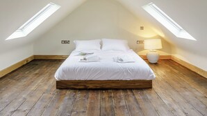 Un dormitorio con techo inclinado, tragaluces, estructura de cama de madera, lámpara de noche y una mesita de noche pequeña.