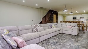 Una sala de estar con un sofá modular, un comedor con sillas de madera, y una cocina al fondo.