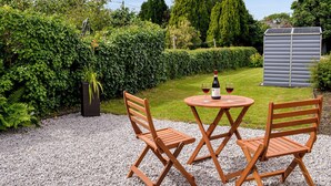 A garden patio with a table and two chairs, a bottle of wine, and a shed in the background.