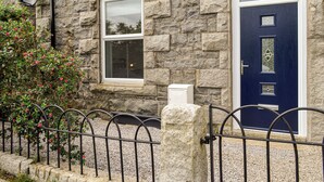 A stone house with a dark blue door, a window with blinds, and a metal fence.