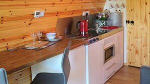 Una cucina compatta con pareti e piano di lavoro in legno, un bollitore rosso, un lavello e un piccolo forno.