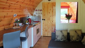 Un accogliente interno di una baita con soffitto in legno, angolo cottura con lavello e fornelli, tavolo da pranzo con sedie e finestra vista su spazi verdi.