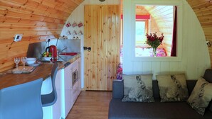 Interno accogliente di una baita con soffitto in legno, angolo cottura con lavello e fornello, e zona salotto con cuscini.