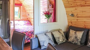 Una camera accogliente con soffitto in legno curvo, un letto con copripiumino floreale, una finestra con vista e un’area salotto con cuscini.