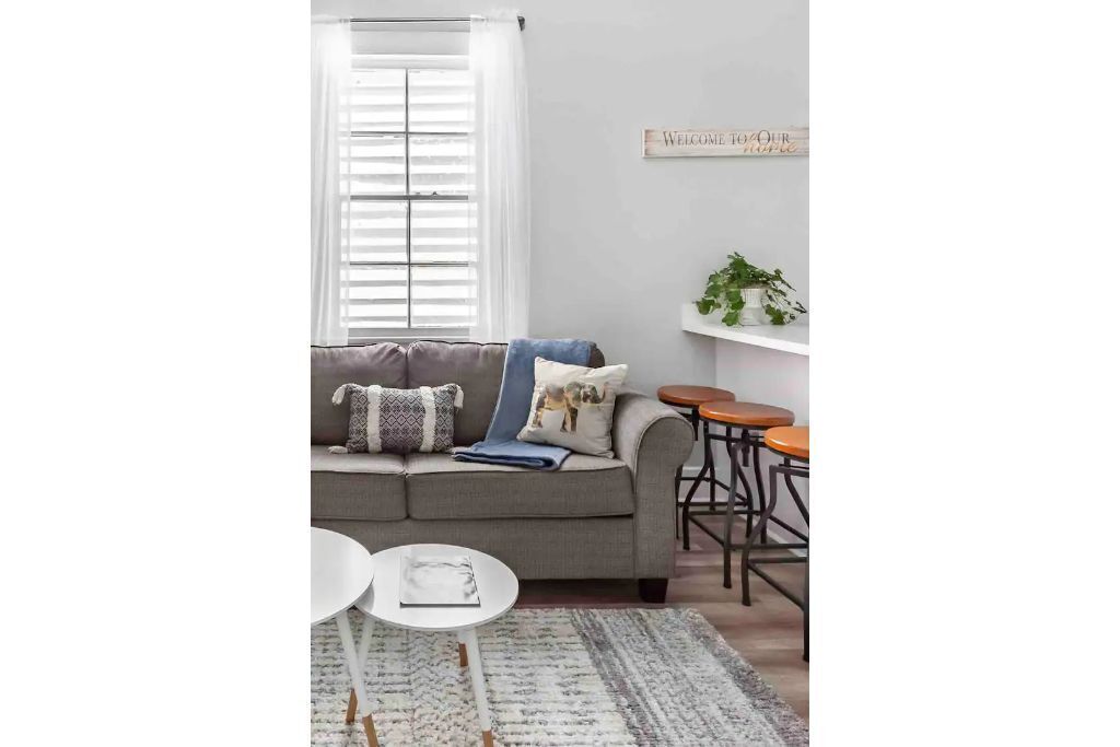 A living room with a grey sofa, a small round table, a white coffee table, and a plant on a shelf.