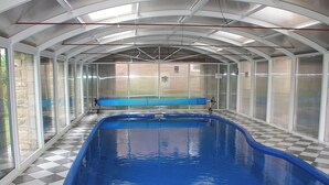 Una piscina coberta amb un paviment d'escacs, vora blava i una estructura de vidre amb teulada metàl·lica.