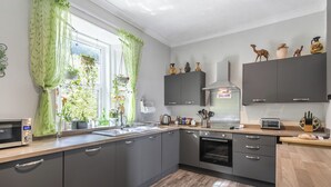 Une cuisine moderne avec des meubles gris, une hotte en acier inoxydable, un four encastré et une fenêtre agrémentée de rideaux verts.