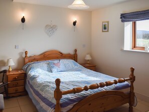 Quarto com cama de madeira, mesa de cabeceira com luminária, luminária na parede e janela com vista para o exterior.
