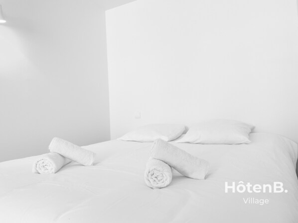 Et hotelværelse med en pænt redt seng, to puder og to sammenrullede håndklæder.