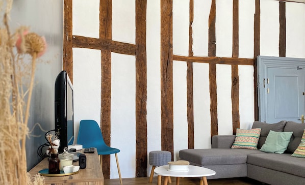 A living room with exposed wooden beams, a grey sofa, a blue chair, and a small white table.