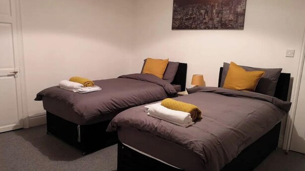 Habitación de hotel con dos camas, cada una con una colcha gris y una toalla amarilla.