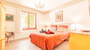 Een lichte slaapkamer met een groot bed, een kroonluchter en een raam met gordijnen.
