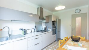 Een compacte keuken met moderne apparatuur, een eethoek met gele stoelen en een klok aan de muur.