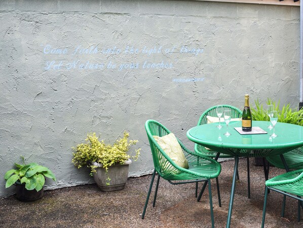 An outdoor seating area with green wicker chairs and a table, a bottle of champagne, and potted plants.