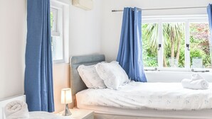 Un dormitorio con cama, mesita de noche, lámpara y ventana con cortinas.