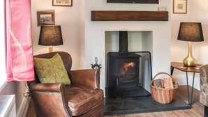 Una sala de estar con chimenea, un televisor montado encima y un sofá de cuero marrón con un cojín verde.
