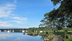 Un lago tranquilo con barcas, un camino de piedra y árboles.