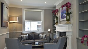 A living room with a sofa, two armchairs, a coffee table, a fireplace, a floor lamp, and a window.