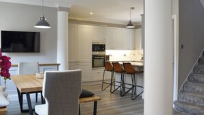 A modern kitchen with white cabinets, a built-in oven, and a dining area with a wooden table and chairs.