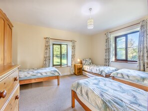 Une chambre avec deux lits simples, une commode en bois, une table de chevet avec une lampe et une fenêtre avec des rideaux.