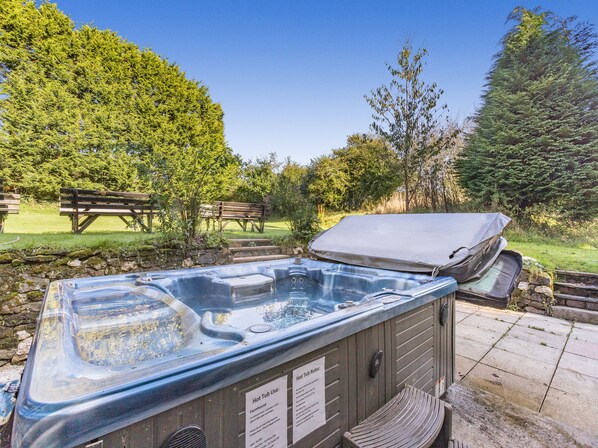 Un bain à remous installé à l’extérieur, avec une terrasse en bois, un banc et une table de pique-nique en arrière-plan.