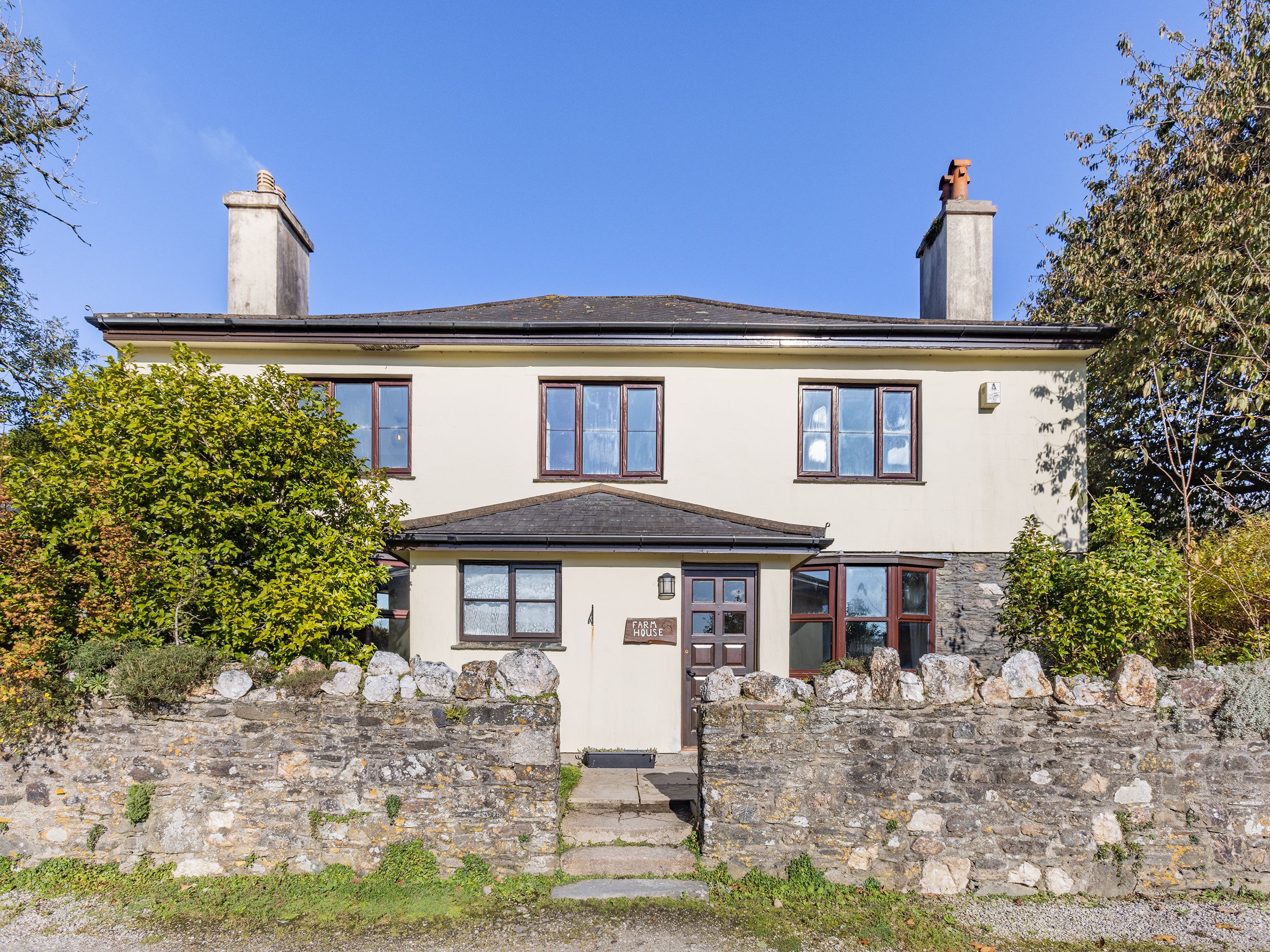 A two-story stone house with a traditional design, featuring a stone wall entrance, multiple windows, and a chimney.