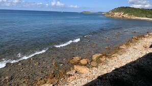 Un paysage côtier caractérisé par une eau limpide, une côte rocheuse et des collines lointaines.