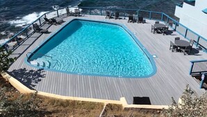 Une piscine entourée d’une terrasse en bois et dotée de chaises longues, avec vue sur l’océan.