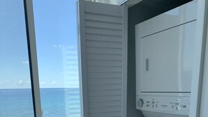 Une buanderie avec vue sur l’océan, un lave-linge blanc et une petite poubelle.
