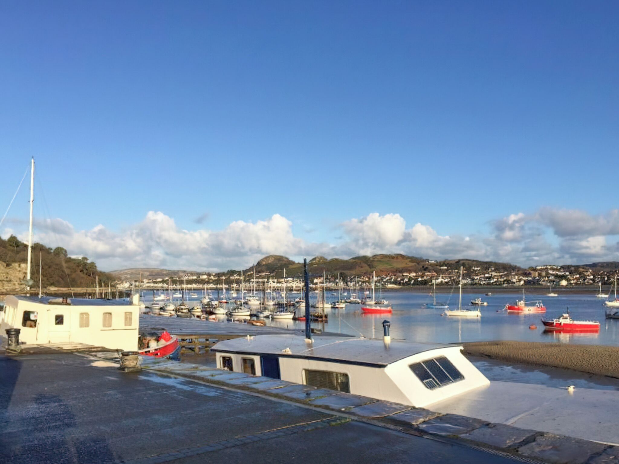 A marina with boats docked, a small building, and a hilly landscape in the background.