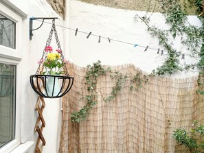 A hanging flower pot with a variety of flowers, a bamboo fence, and a string of clothespins on a wall. - 2 bedroom accommodation in Conwy (Conwy)