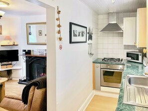 A compact kitchen with a gas stove, oven, microwave, and a sink. There's a framed picture on the wall and a small shelf with a lamp. - 2 bedroom accommodation in Conwy (Conwy)