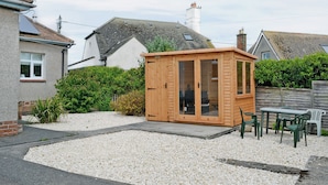 Un invernadero de madera con puertas de cristal, un patio de grava y una zona de estar con sillas de plástico.