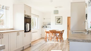 Una cocina moderna con armarios blancos, una mesa de comedor de madera y un horno empotrado.