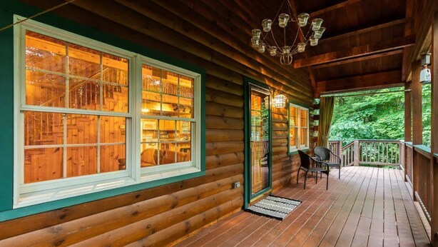 A log cabin with large windows, a porch, and a chandelier.