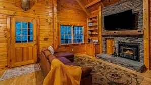 A cozy log cabin interior with a fireplace, wooden walls, and a comfortable seating area.
